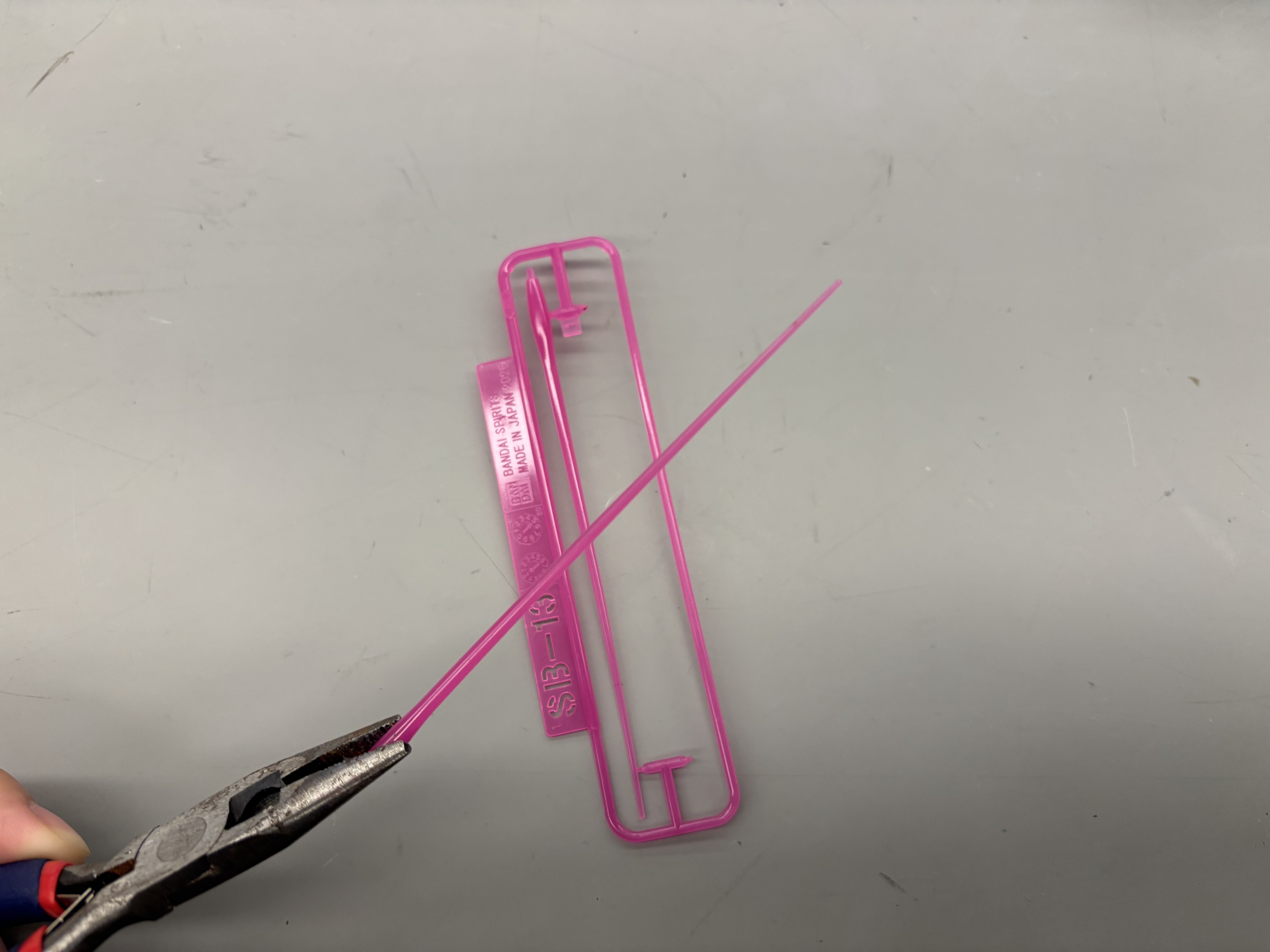 SB-13 rigid styrenic runner sample held in tweezers.